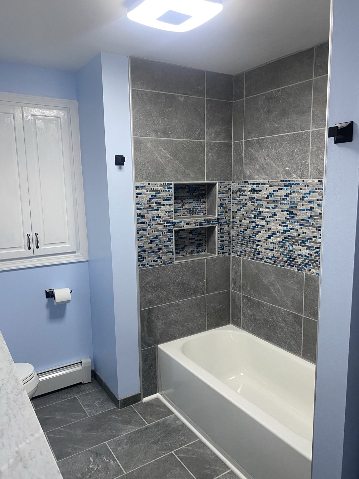 Renovated bathroom with gray tile, blue mosaic accent, bathtub and new flooring
